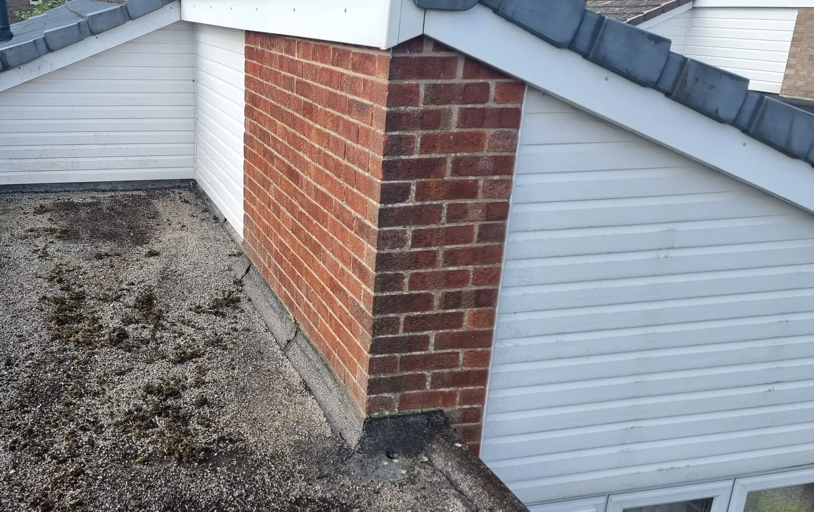 The old felt roof in Sleaford, covered in loose stone chippings and moss, with a cracked felt upstand against the brick pier