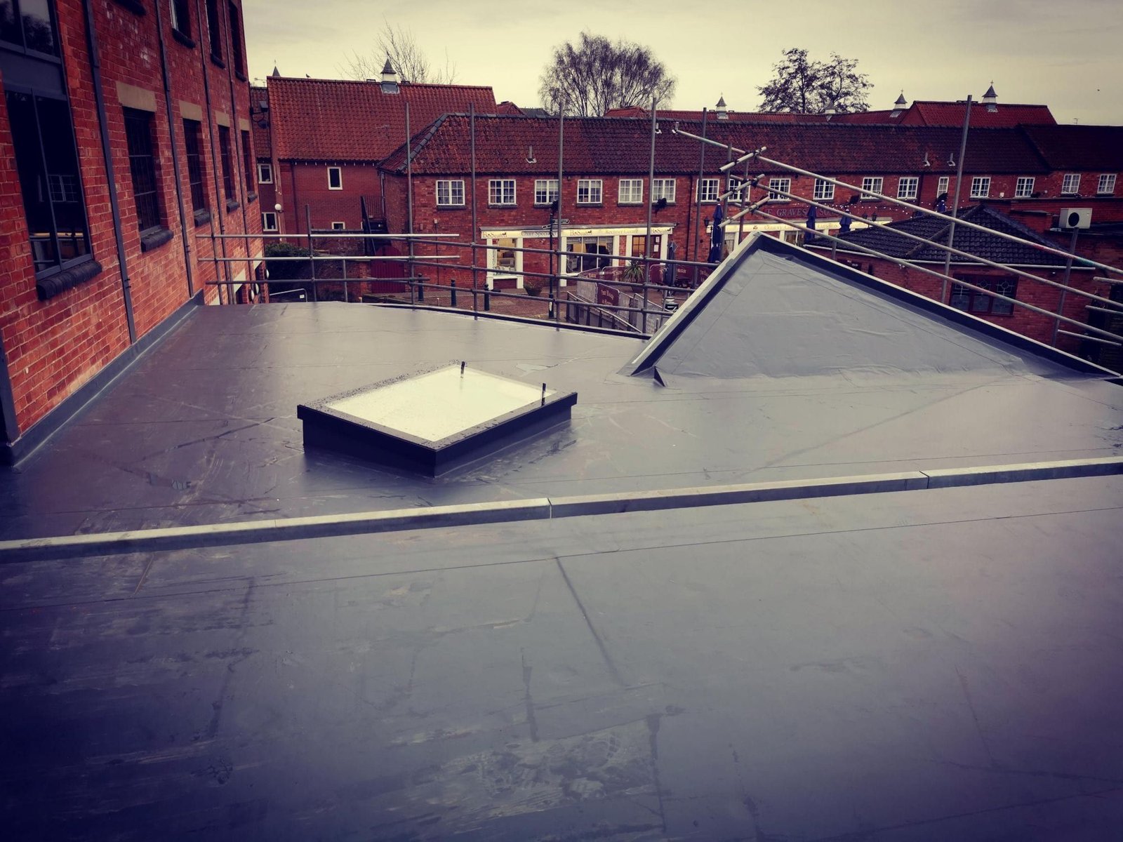 A finished grey single ply flat roof in Sleaford, Lincolnshire, with a rooflight and a hipped section, among red-brick shops and offices